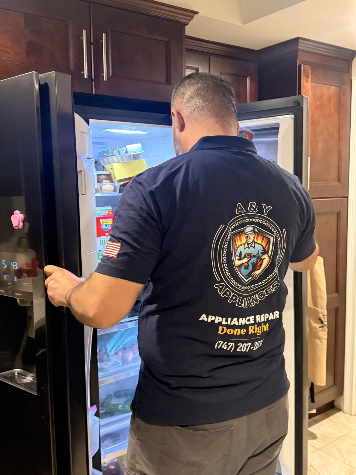 A&Y Appliances technician in branded uniform diagnosing a refrigerator on a service call
