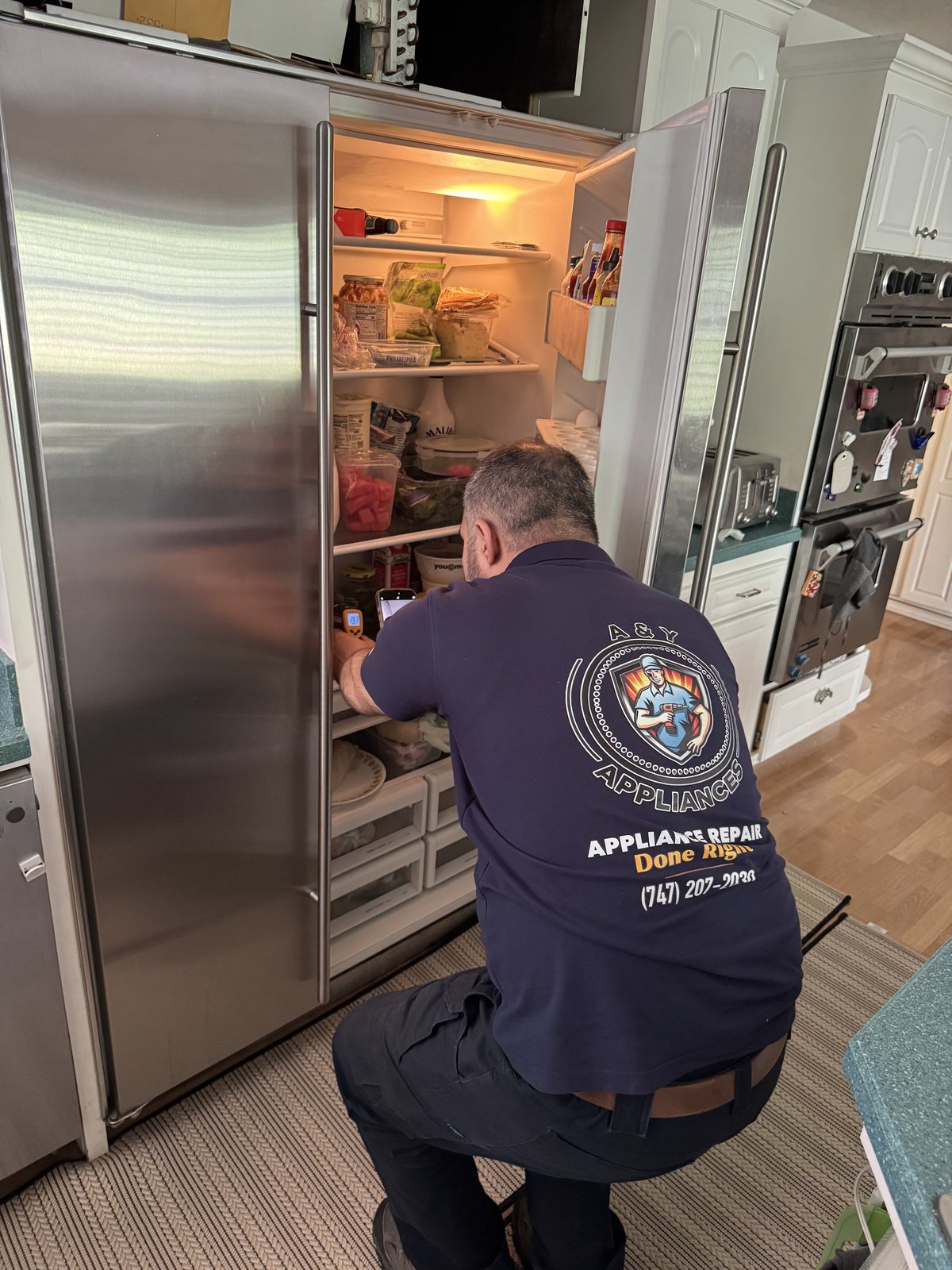 A&Y Appliances technician verifying temperatures inside a built-in Sub-Zero refrigerator with an infrared thermometer