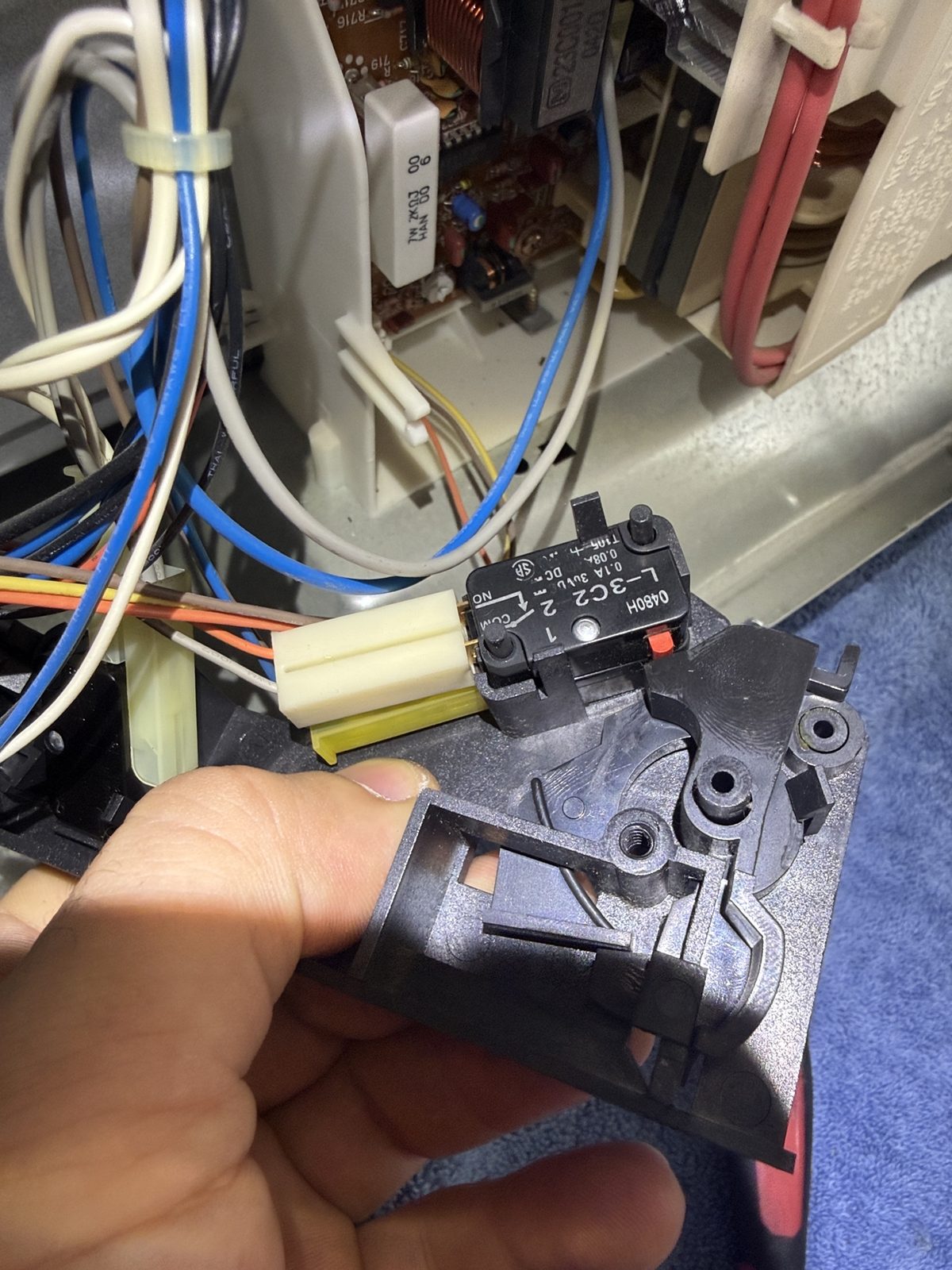 Technician holding the disassembled door latch assembly with interlock switch from a built-in Thermador microwave during repair